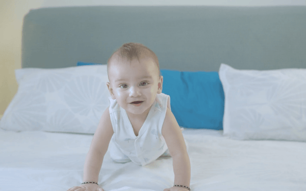 Smiling baby crawling on white bed with blue and white pillows in bedroom
