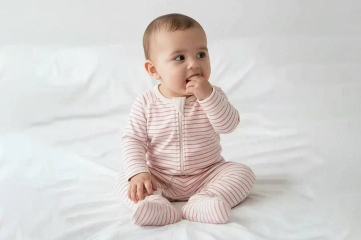 Baby wearing a soft organic cotton pink striped romper sitting on a white blanket.