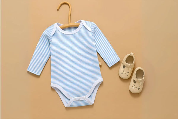 Blue and white striped long-sleeve baby onesie on hanger with beige baby shoes on tan background