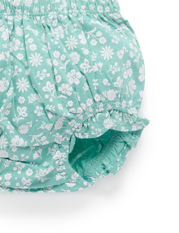 Close-up of teal baby bloomers with white floral print and elastic waistband and leg openings