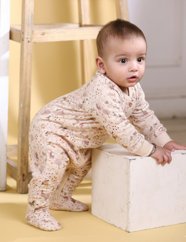 Baby wearing a beige quilted full-sleeve romper with farm-themed print, standing while holding a white box in a cozy indoor setting