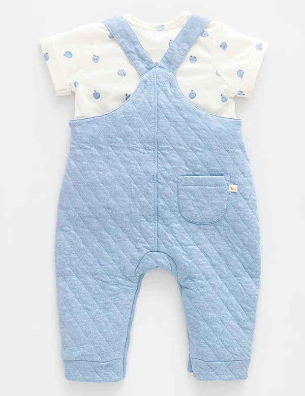 Back view of light blue quilted baby dungarees with a white short-sleeve shirt featuring blue apple prints