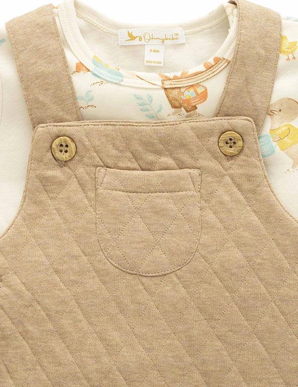 Beige quilted dungaree with buttons and a white shirt with colorful design underneath.