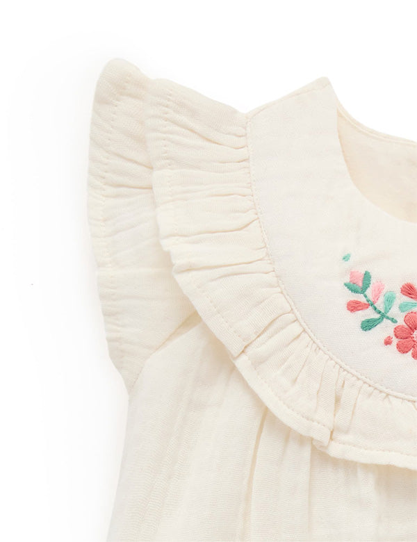 Close-up of cream baby girl frill sleeve top made from soft organic cotton.
