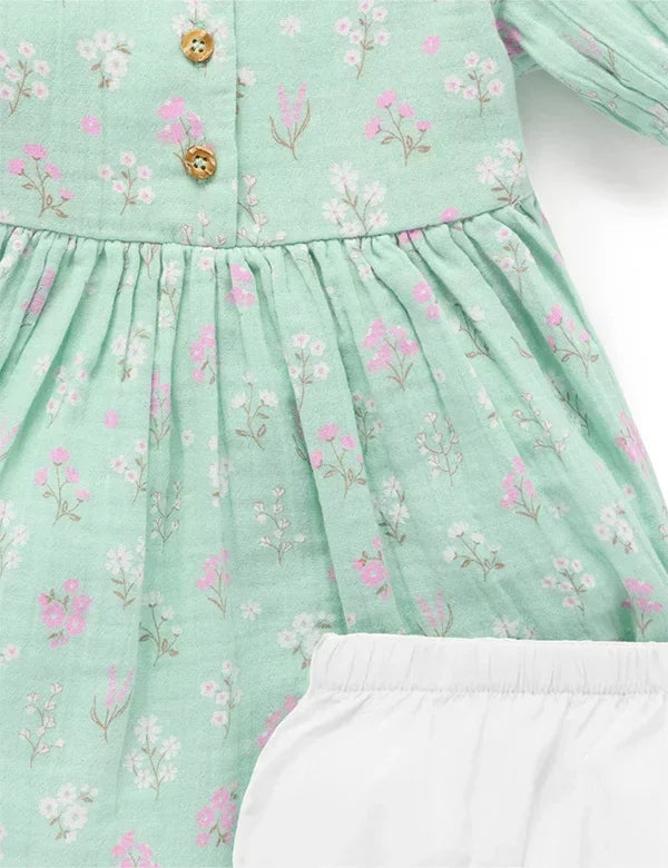 Close-up of mint green baby dress with pink and white floral print and wooden buttons, paired with white bloomers