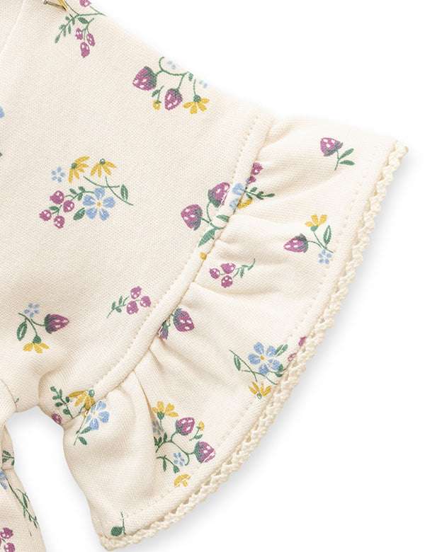 Close-up of flutter ruffle sleeve with delicate floral print on cream baby romper. 
