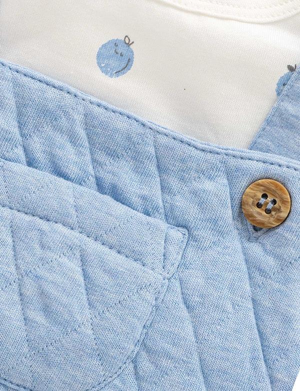 Close-up of light blue quilted baby dungarees with wooden button and white fabric with blue prints