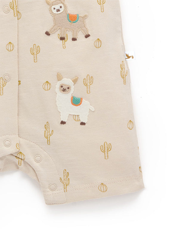Close-up of beige baby romper with llama and cactus embroidery and snap buttons