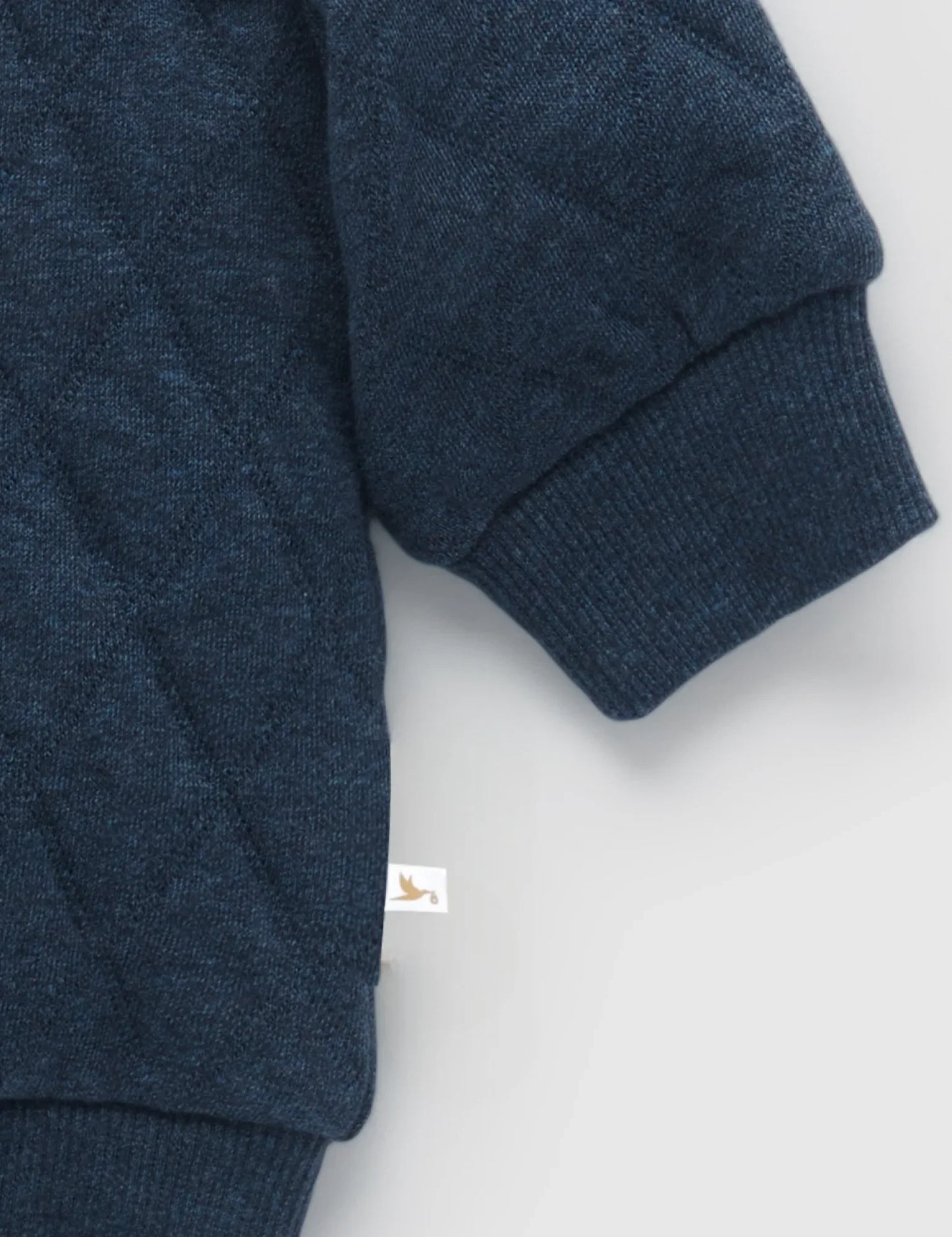 Close-up of navy blue quilted baby sweater sleeve with ribbed cuff on gray background