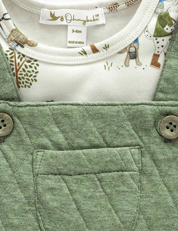 Close-up of olive green quilted baby dungaree with wooden buttons and printed white cotton shirt