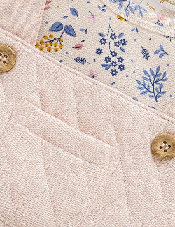 Close-up of pink quilted baby dungaree with buttons and floral patterned inner lining