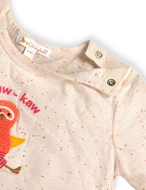 Close-up of speckled baby T-shirt with snap buttons and embroidered bird design in soft beige fabric