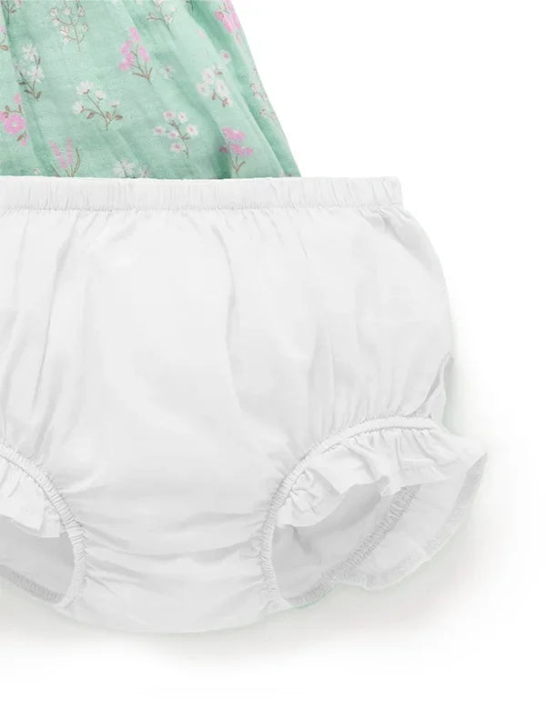 Close-up of white baby bloomer with elastic waist and ruffled leg openings on floral fabric background