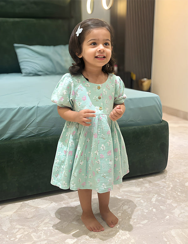Little girl wearing a seafoam floral printed organic cotton baby dress standing indoors