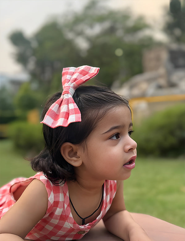 Little girl wearing coral gingham summer dress posing out doors