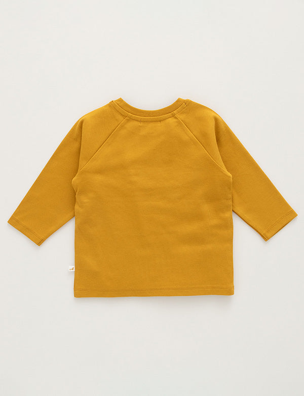 Back view of mustard organic cotton long sleeve baby top on neutral background