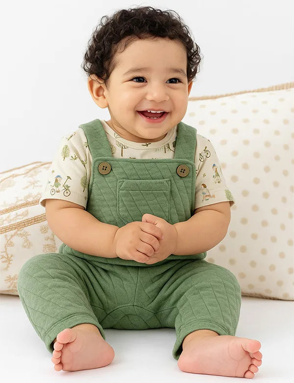 Smiling baby boy wearing an olive green quilted baby boy dungaree with an animal-print tee.