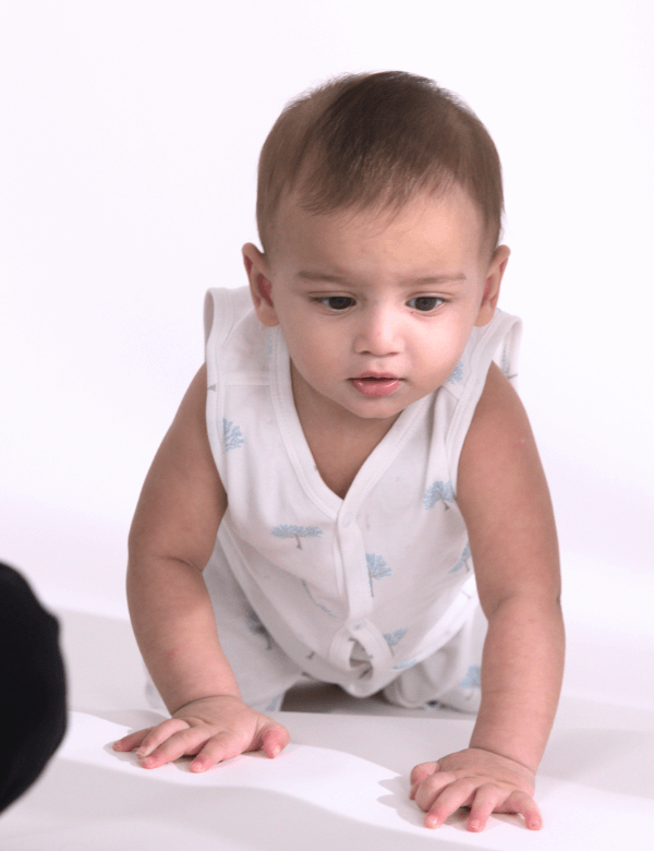 Curious baby crawling on white surface wearing white sleeveless outfit with blue patterns