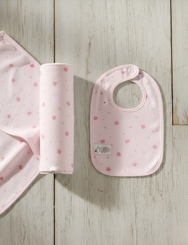 Pink baby bib and changing mat with small pink leaf pattern on light wood background