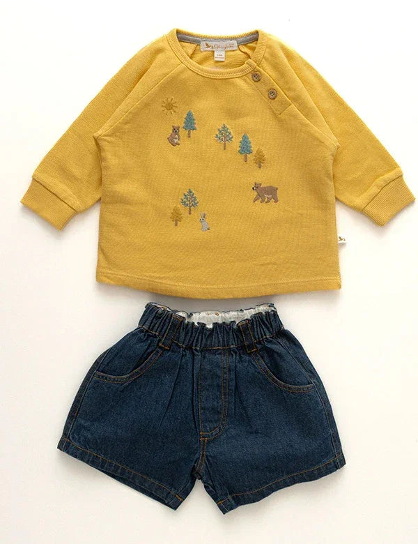 Yellow long-sleeve toddler shirt with forest animal and tree prints paired with dark blue denim shorts