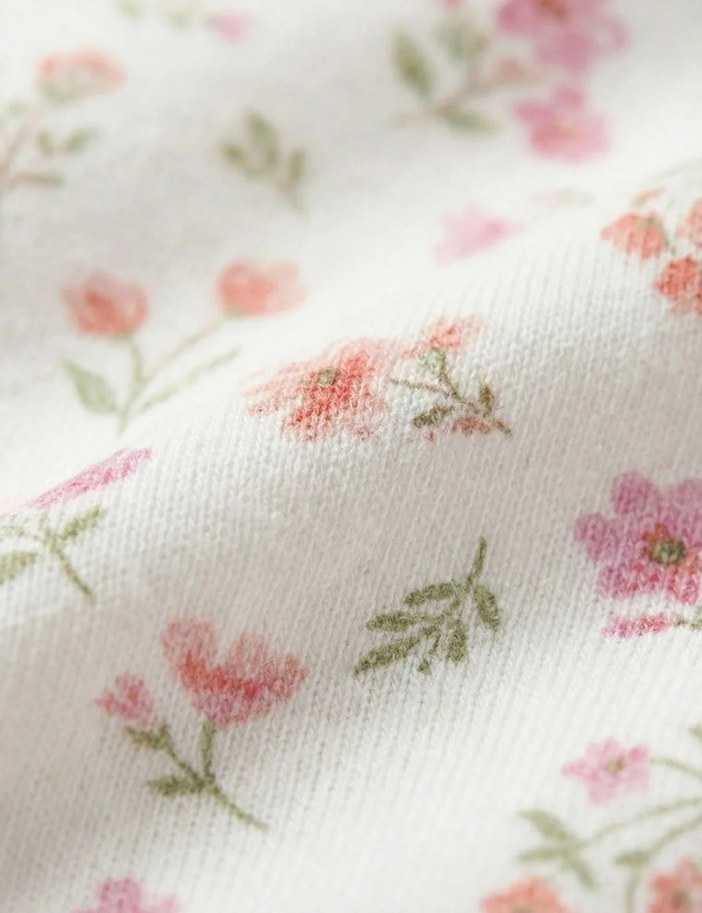 Detailed fabric close-up of the white organic cotton baby growsuit showcasing the delicate pink flowers and small green leaves print.