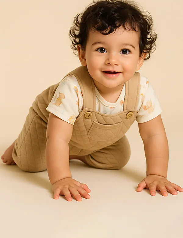 Baby wearing beige overalls and a white shirt with animal prints on a beige background