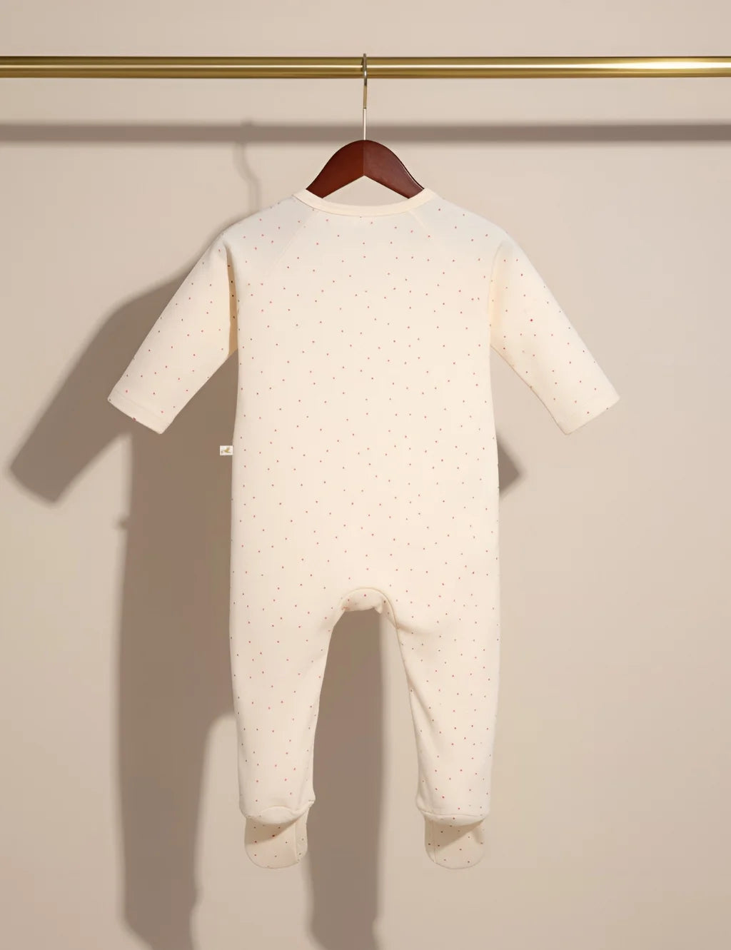 Baby onesie with feet hanging on a wooden hanger against a beige wall.