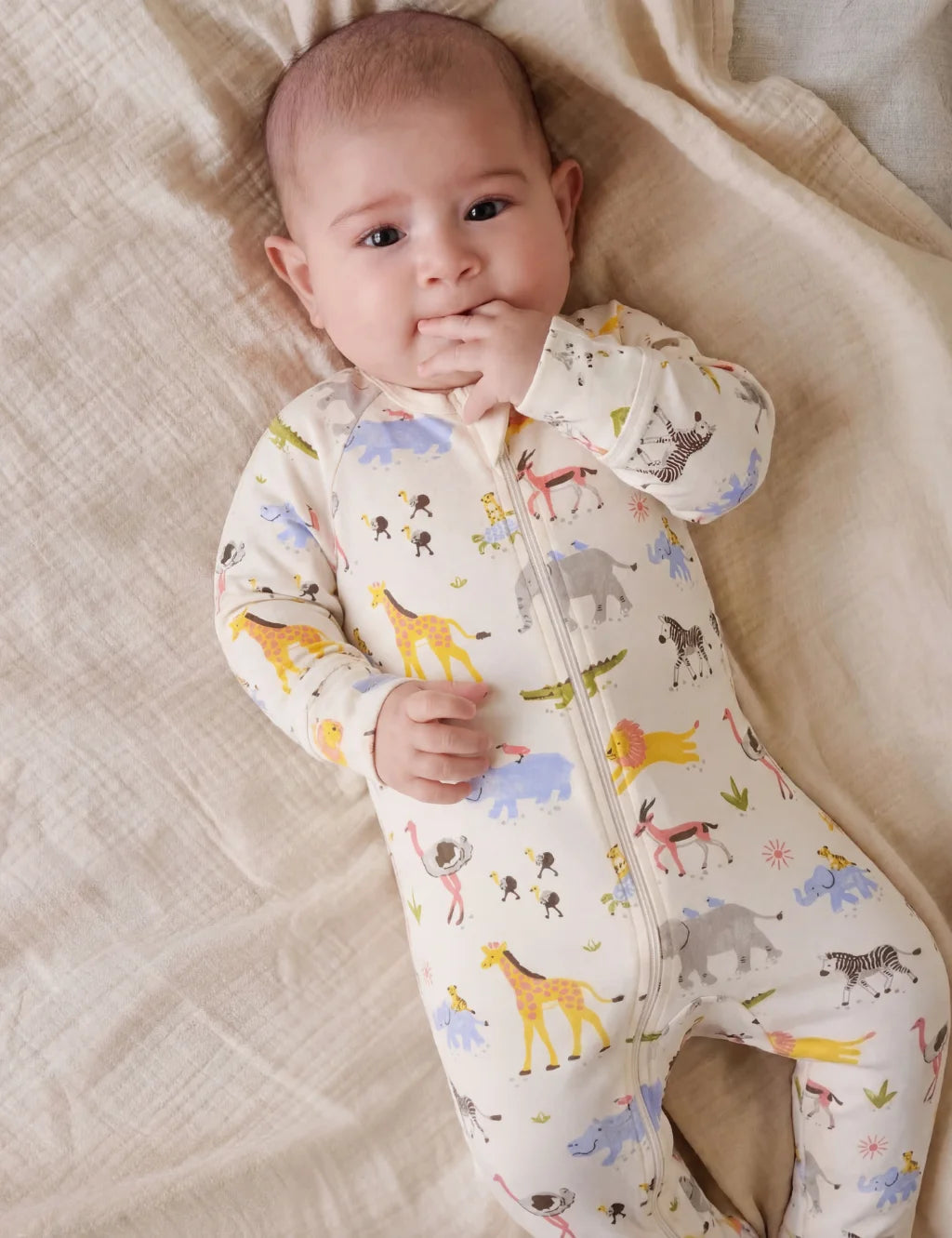 Baby wearing a onesie with animal prints lying on a textured surface