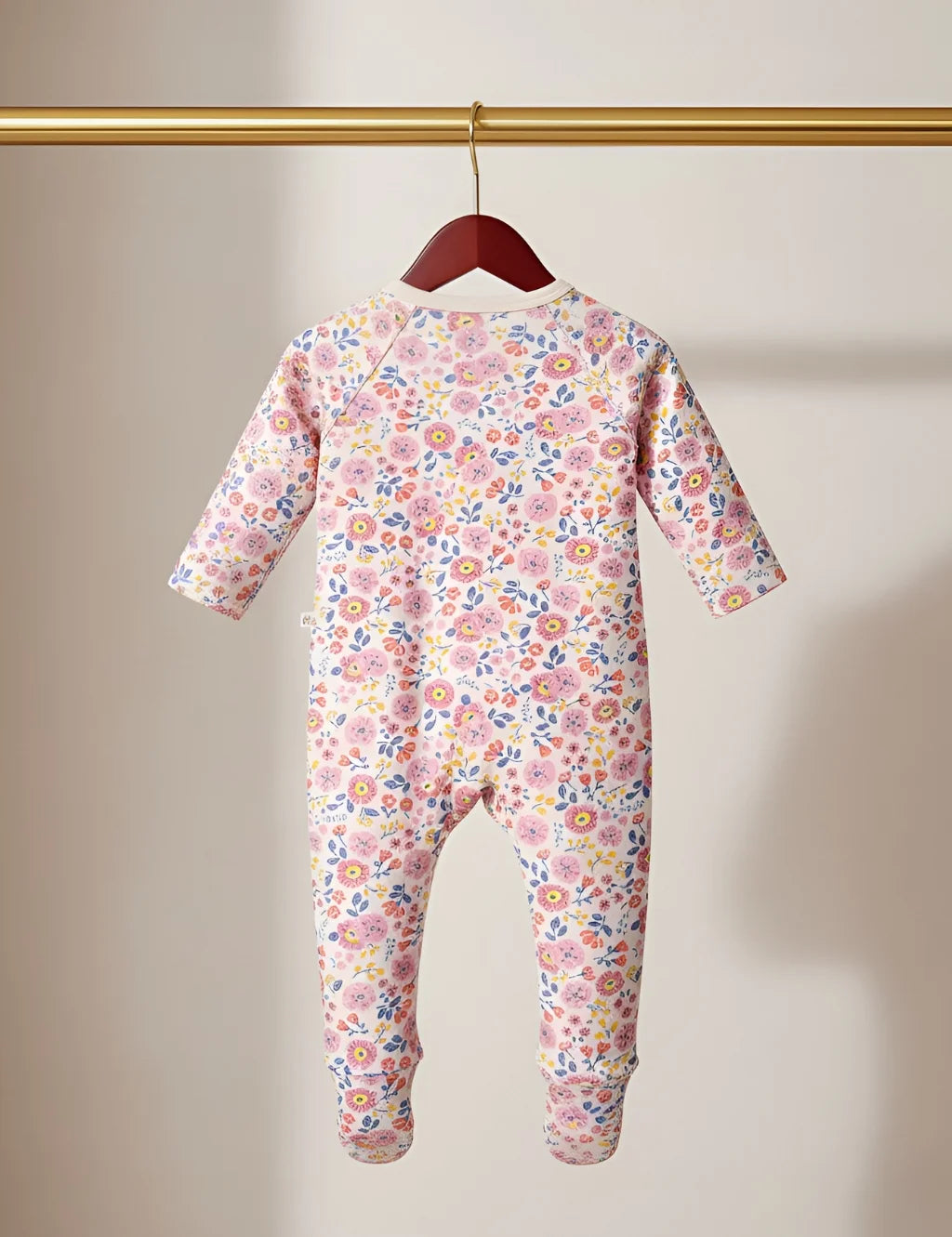 Floral-patterned baby onesie hanging on a wooden hanger against a beige wall.