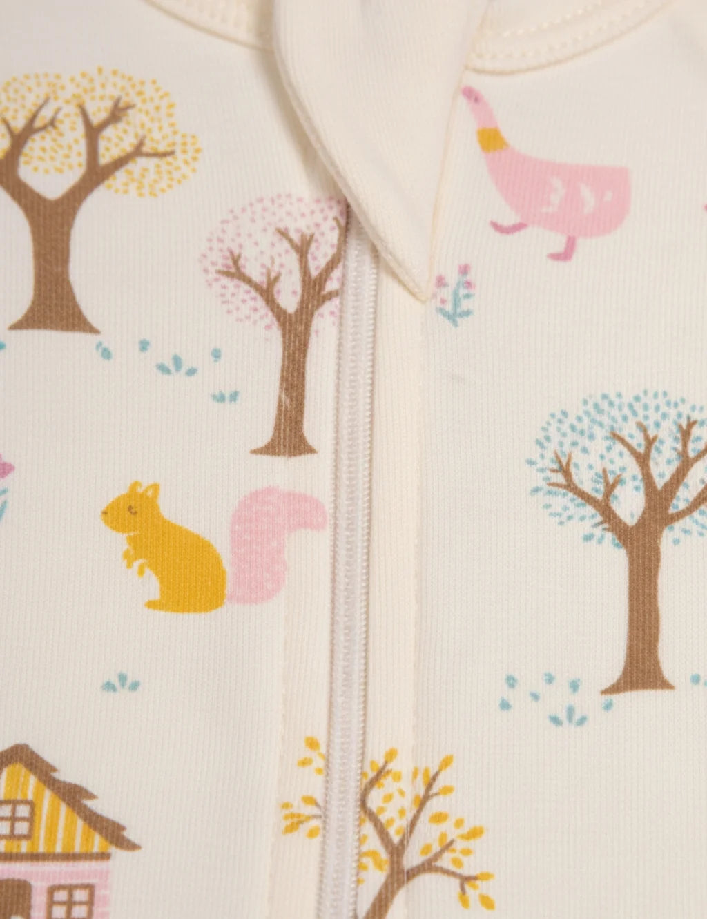 Close-up of a baby romper with forest-themed illustrations including trees, a house, and a squirrel.
