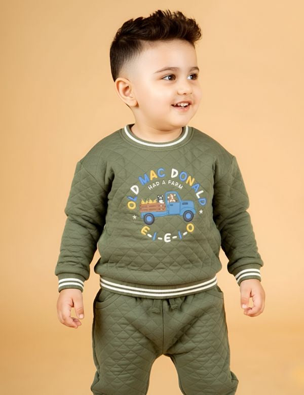 Child wearing a green outfit with a cartoon design on a beige background