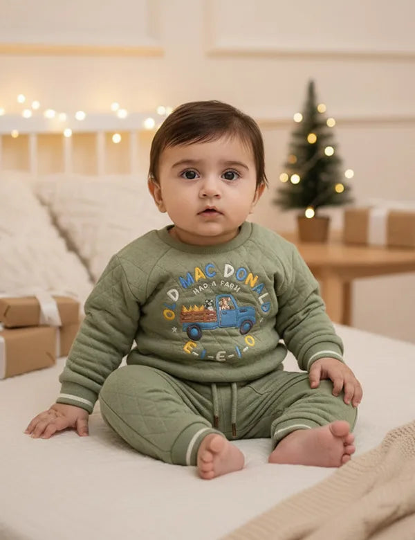 Baby wearing a green outfit with colorful text and graphics, sitting on a light-colored surface.