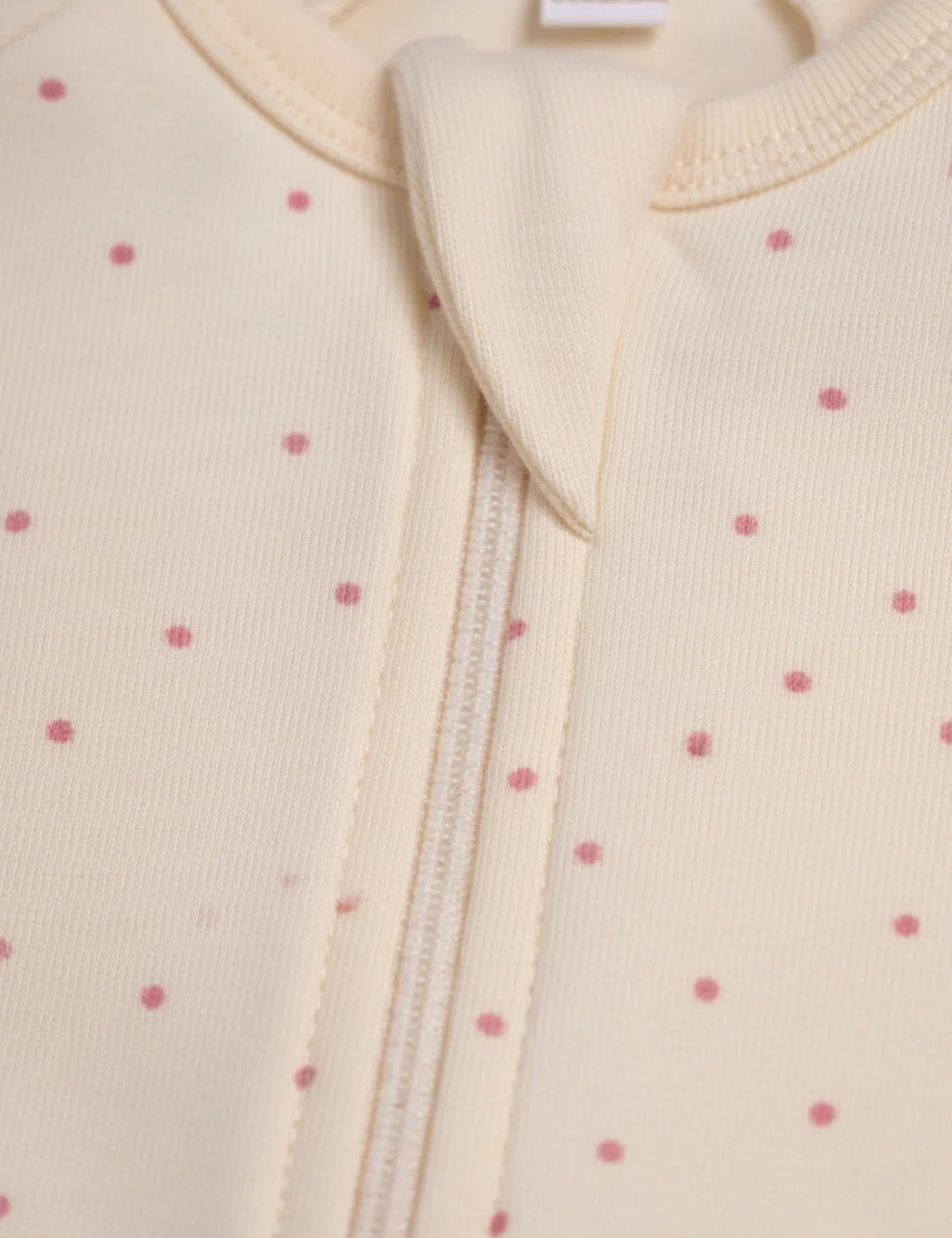 Close-up of a baby outfit with a zipper on a light pink background with small red polka dots.