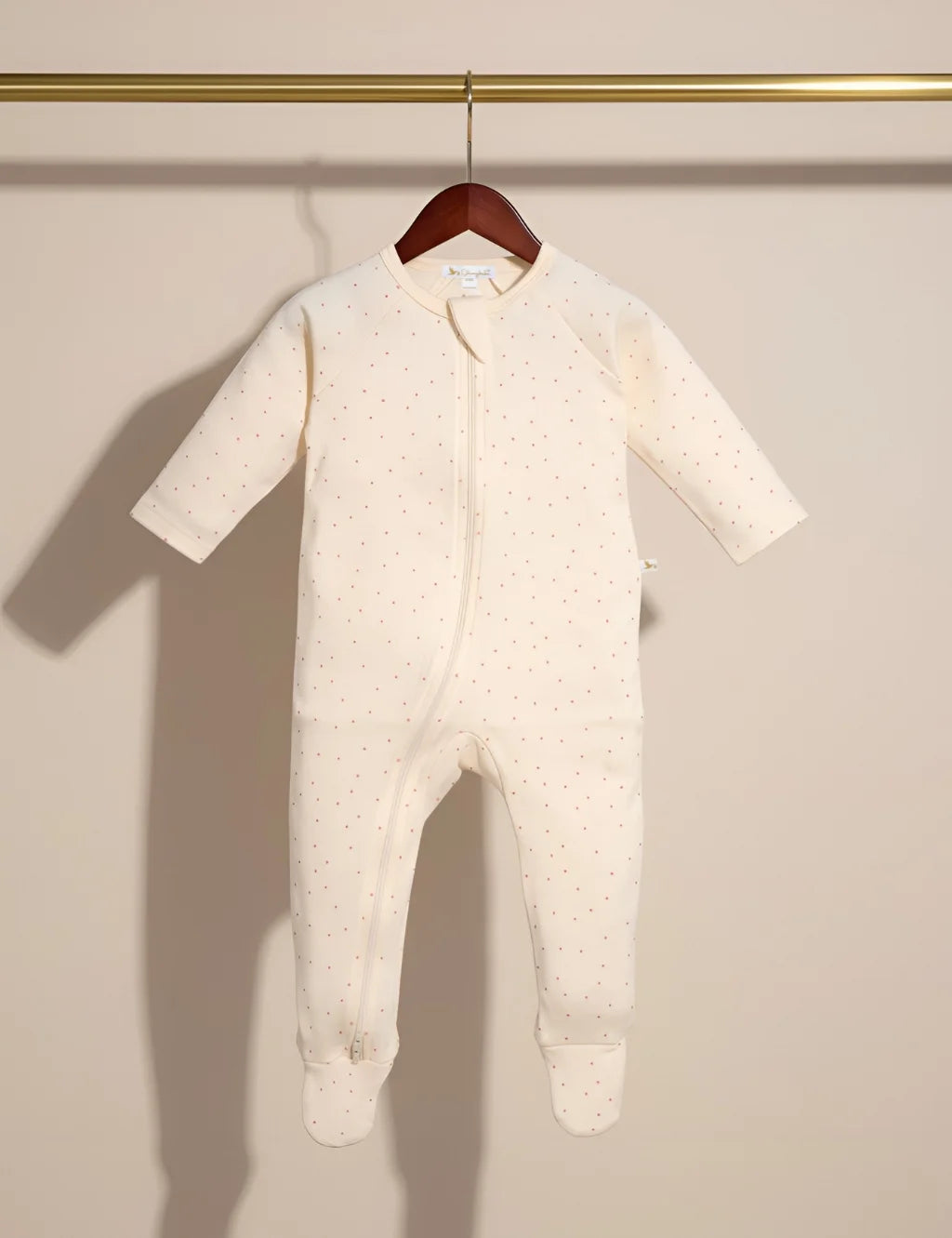 Baby onesie with footies hanging on a wooden hanger against a beige wall.