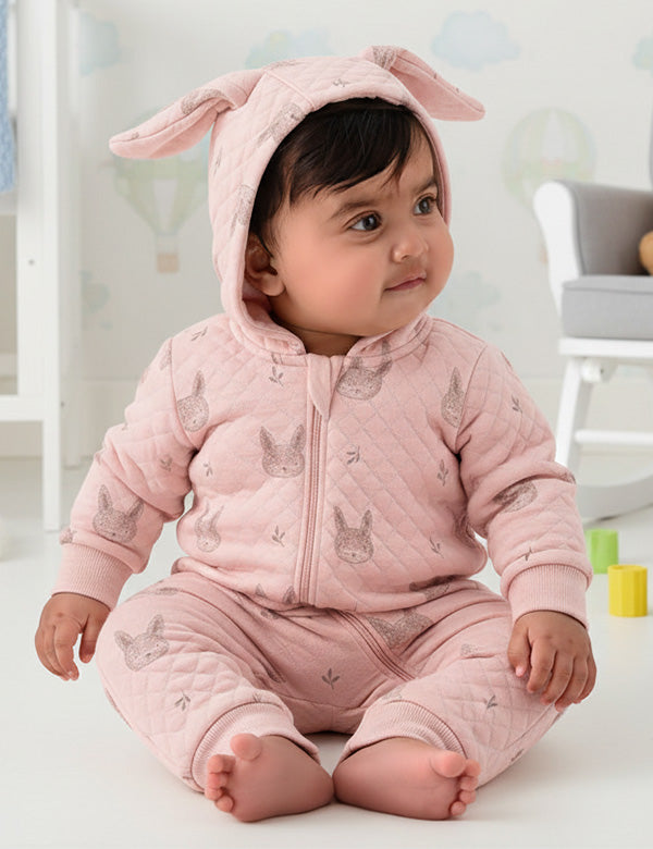 Baby wearing a pink bunny onesie with ears in a bright room.