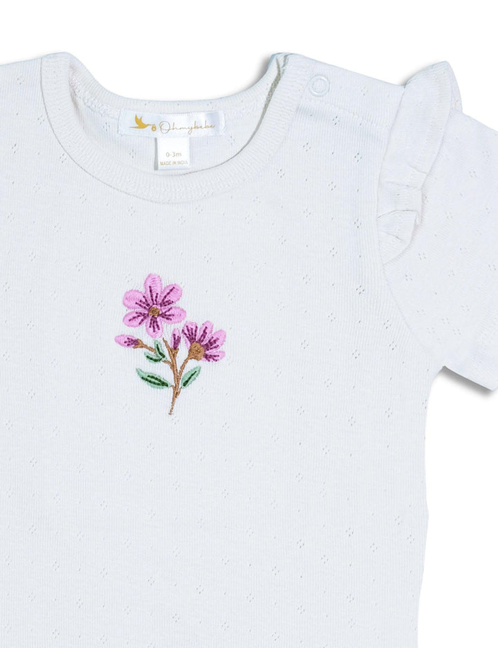 Detailed close-up of the delicate pink and purple floral embroidery on the white baby bodysuit. Shop unique baby clothing India.