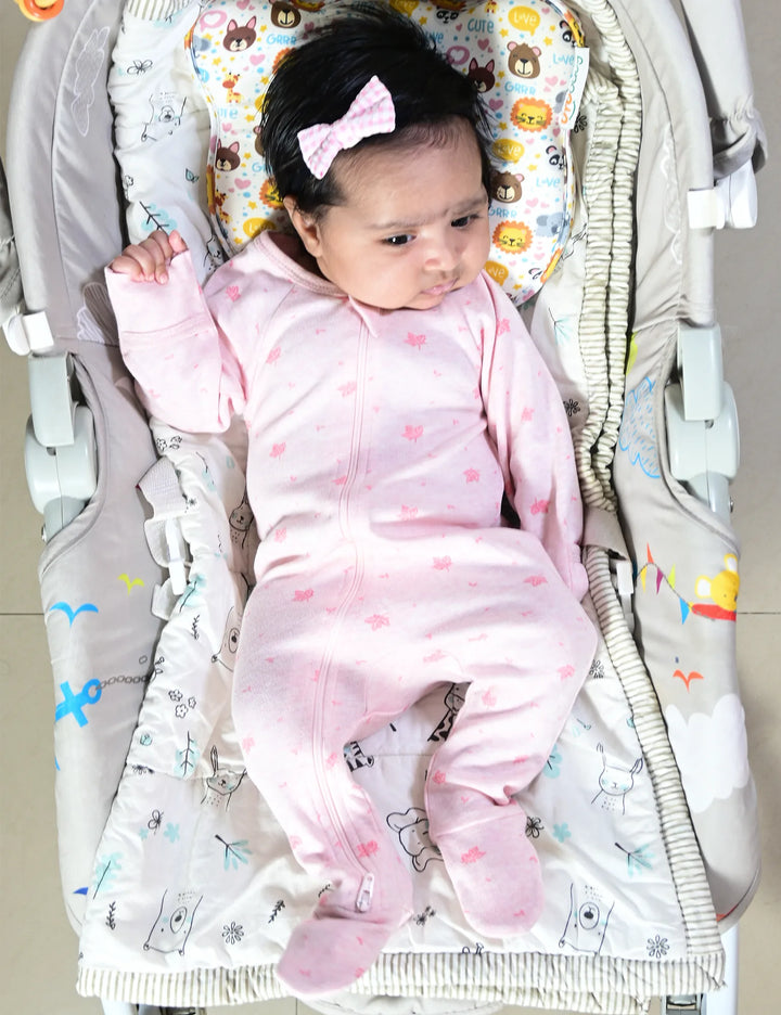 A peaceful baby, who appears to be of South Asian descent, lying in a baby rocker wearing pink leaf print organic cotton footed. Shop cozy baby sleepwear India.