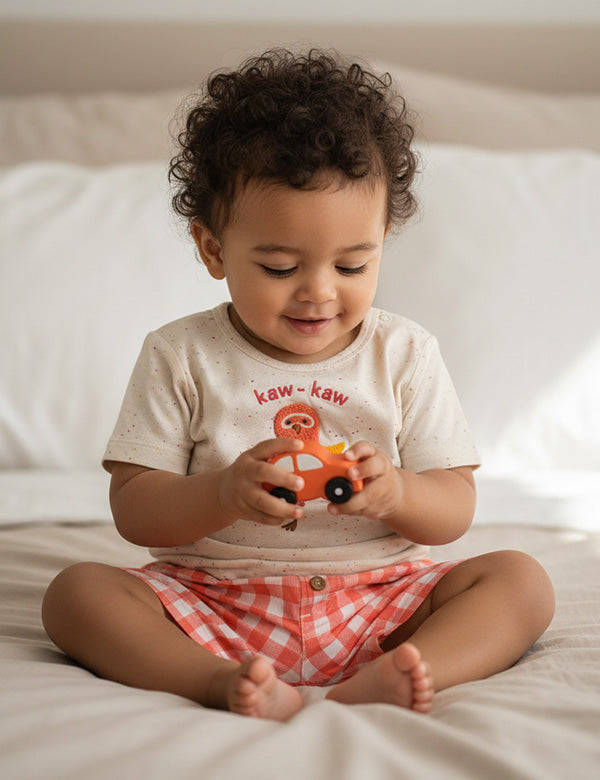 Smiling baby wearing a speckled bird-print T-shirt and peach gingham shorts, organic cotton baby outfit.