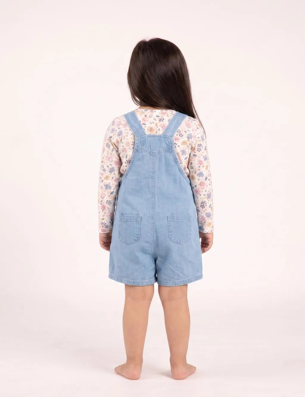 Back view of a toddler girl wearing light wash denim short overall romper with back patch pockets.