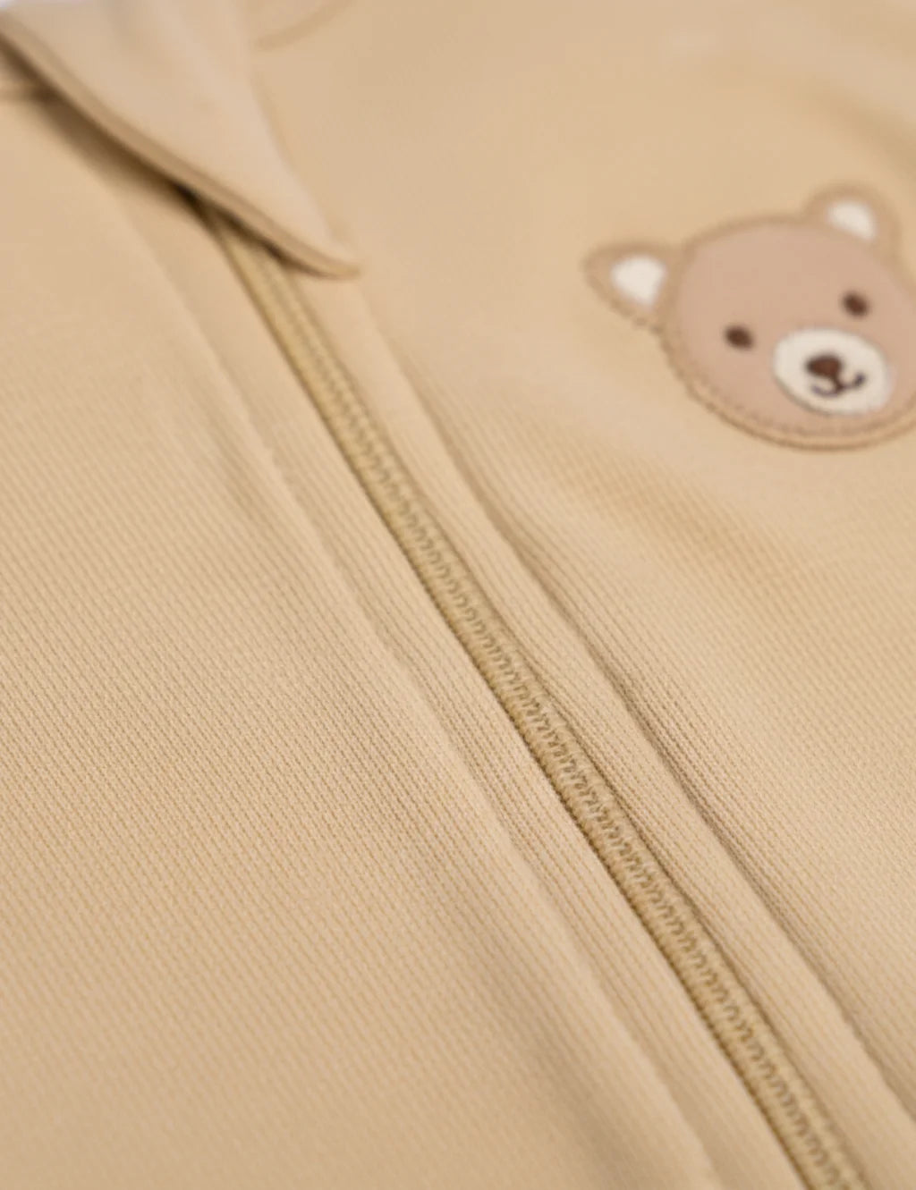 Close-up of a beige jacket with a teddy bear face patch on a beige background
