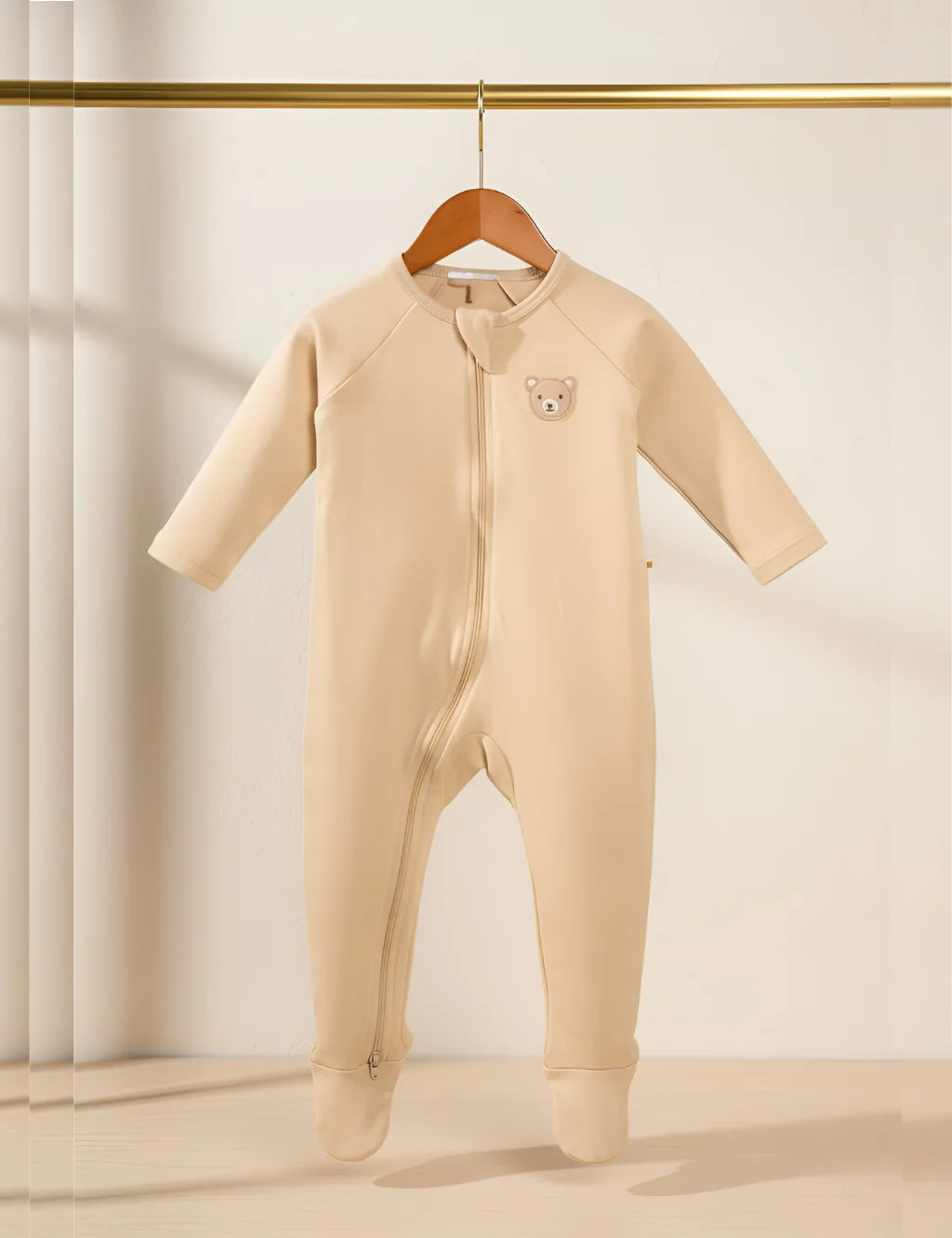Beige baby onesie with a bear patch on a wooden hanger against a neutral background