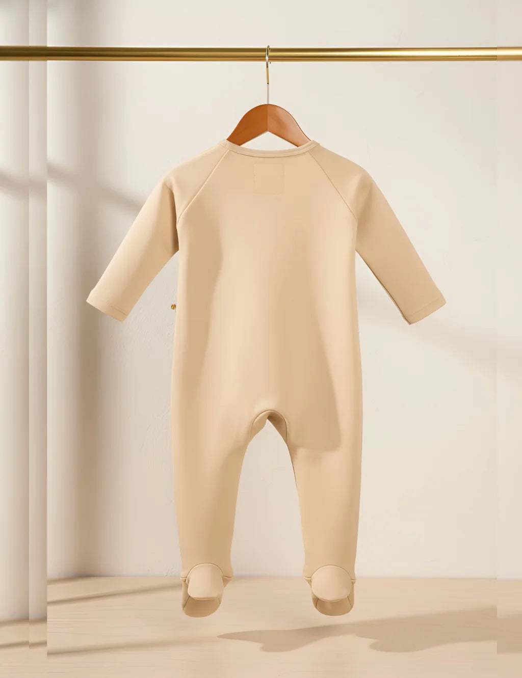 Beige baby onesie on a hanger against a neutral background