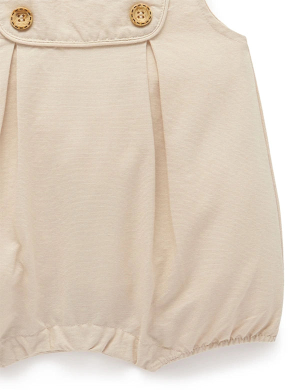 Close-up of beige baby romper with wooden buttons and elastic leg openings in soft fabric