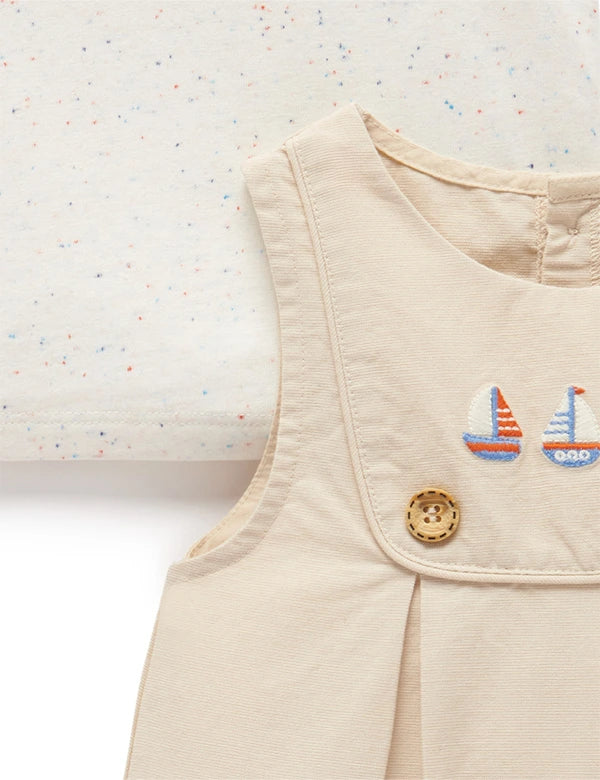 Close-up of beige baby romper with embroidered sailboats and wooden button, paired with speckled cream fabric top