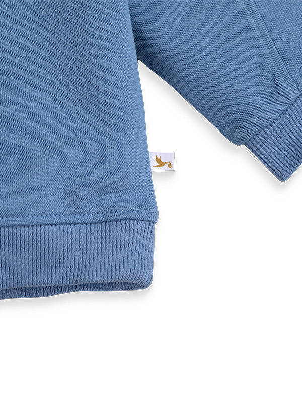 Close-up of blue kids winter sweatshirt sleeve and cuff with small white tag featuring bird logo