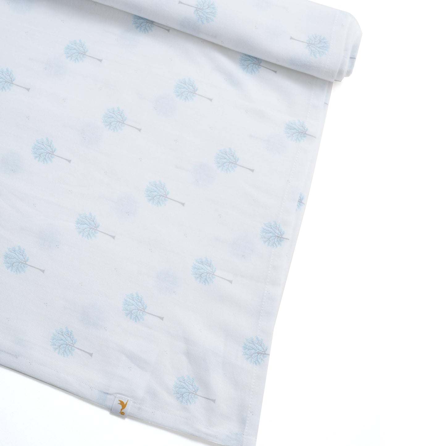 Soft white baby swaddle fabric with light blue tree print, neatly folded edge