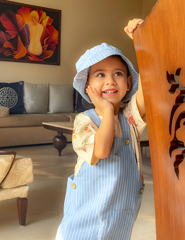 Child in a blue outfit standing in a living room with a couch and decorative pillows.