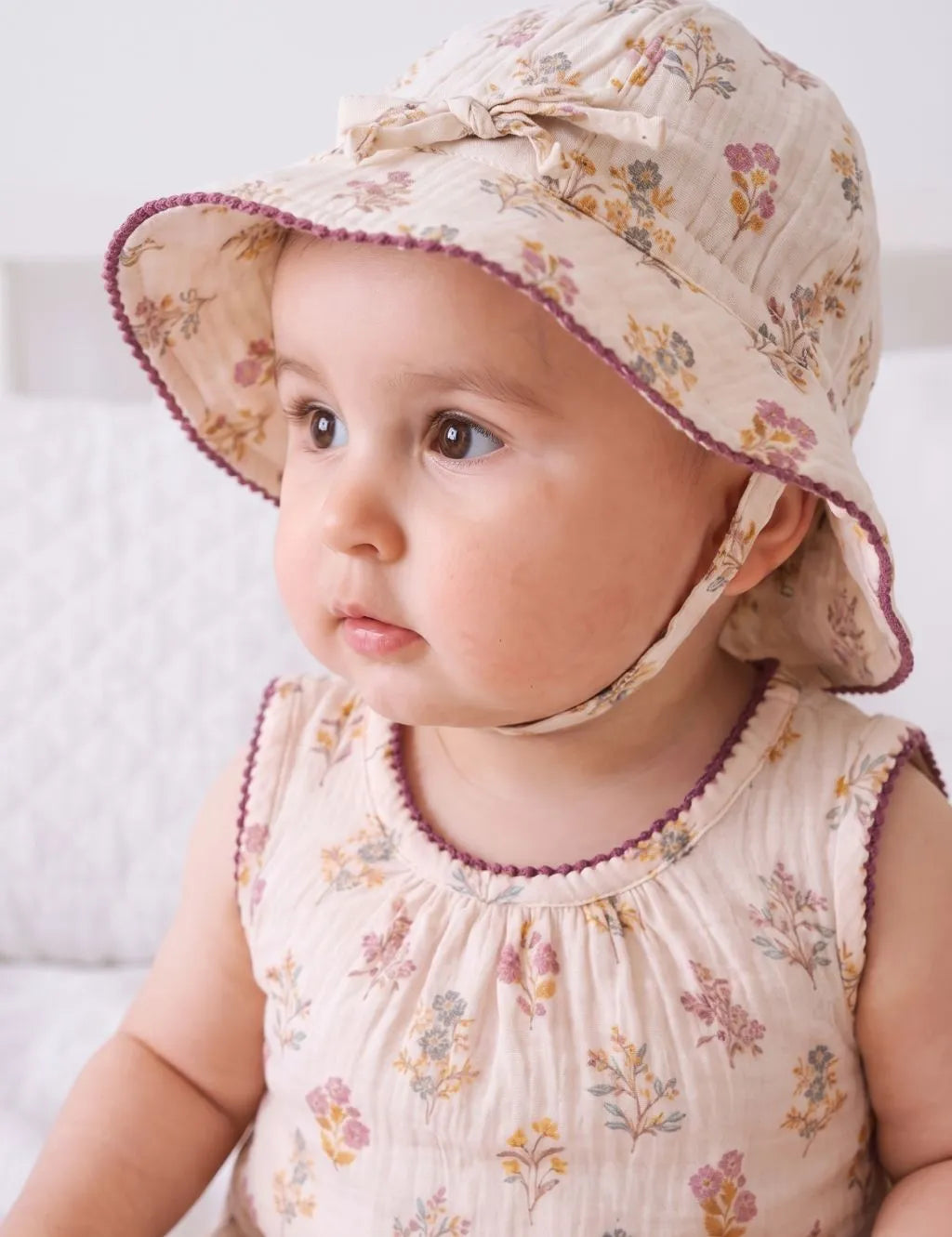 Close-up shot of a baby girl wearing a floral print wide-brim sun hat with chin strap and matching outfit.