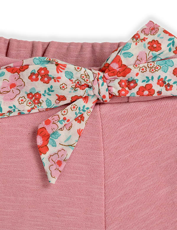 Close-up of pink knit fabric pants with a floral patterned fabric bow tied at the waistband