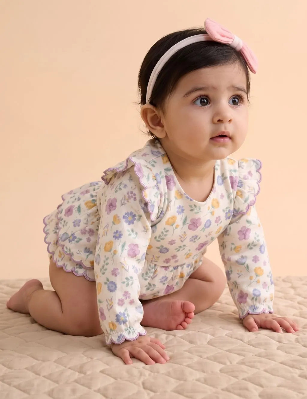Crawling baby girl wearing a floral tiered dress romper with purple scalloped trim and a pink headband.